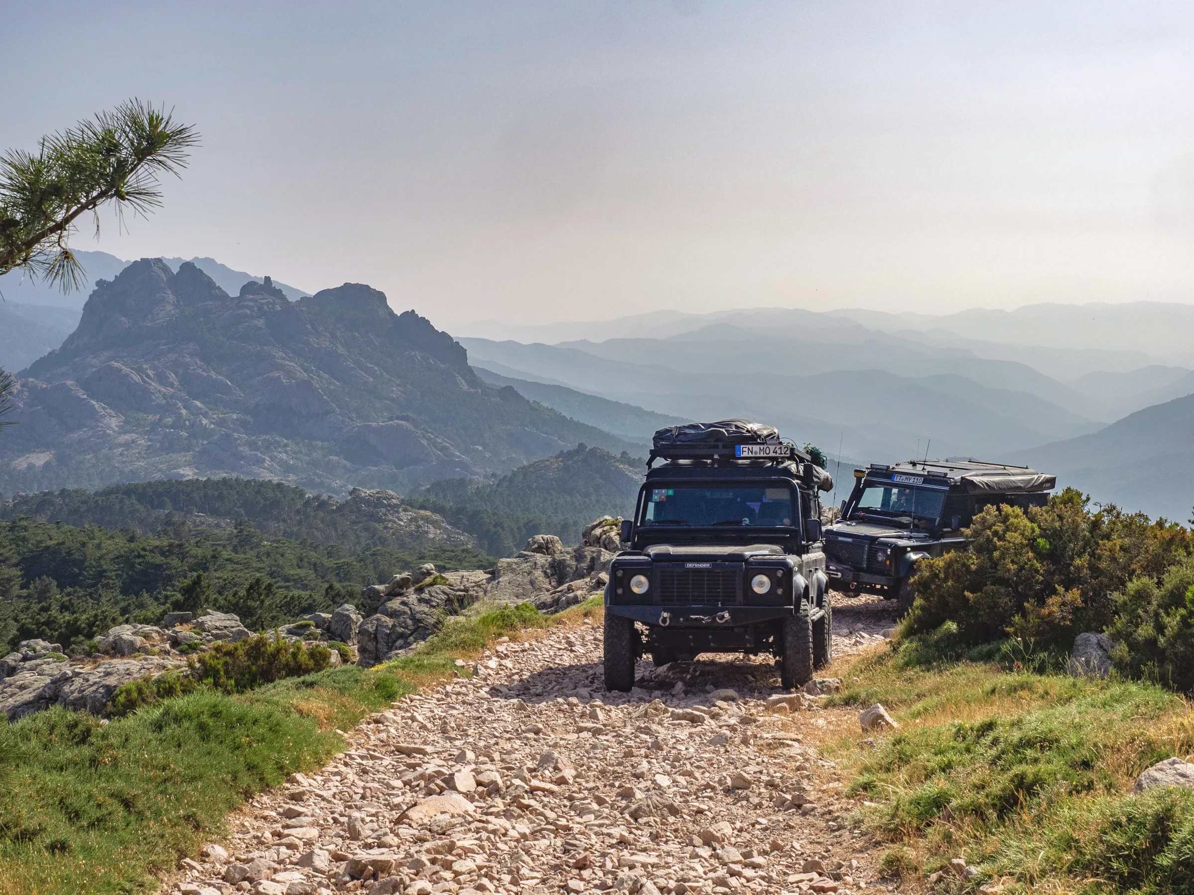 Zwei Land Rover Defender auf einer felsigen Bergpiste über den Bergen Korsikas
