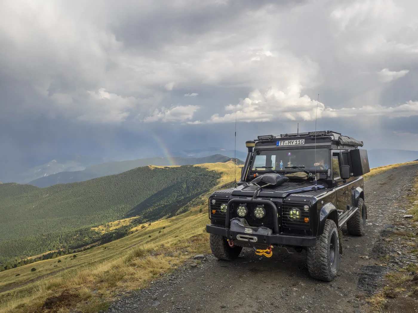 Defender auf einem Bergkamm mit Regenbogen im Tal